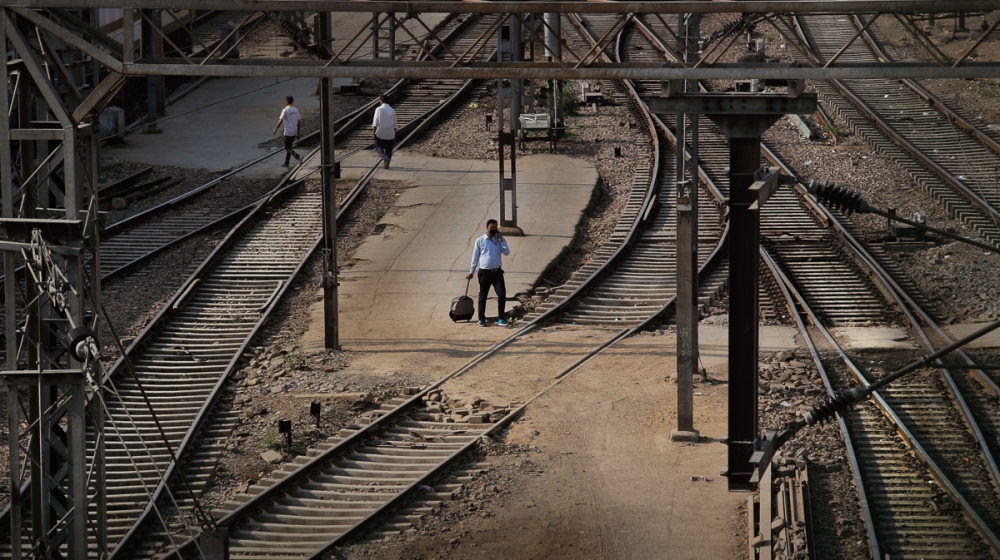 In this Monday, March 23, 2020, photo, a passenger walks past railway tracks at the deserted New Delhi Railway station during a lockdown amid concerns over the spread of Coronavirus, in New Delhi, Ind
