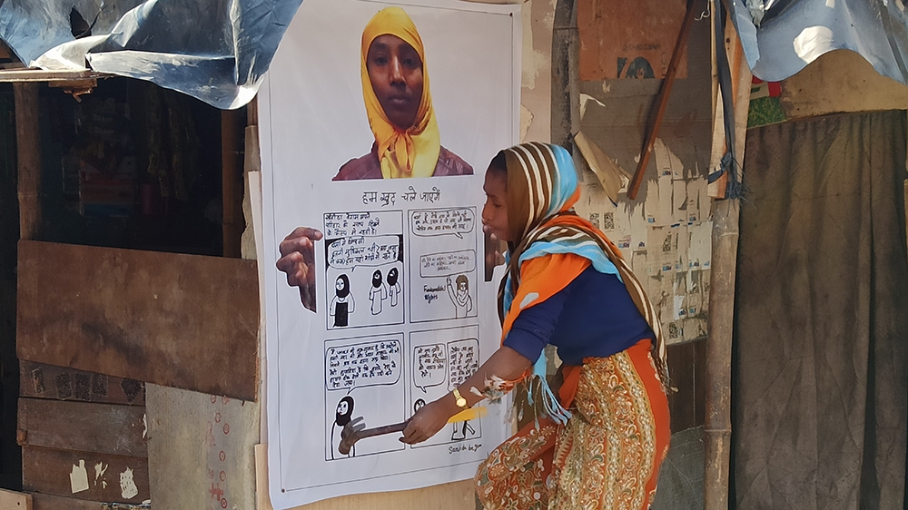 Sanjida Begum pictured left putting up her poster of her comic “ We will return on our own” [Tasnim Nazeer/Al Jazeera]
