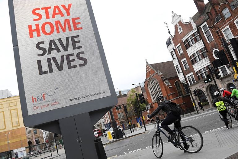 Cyclists pass an electronic billboard displaying a Public health information campaign message from the UK government and local government in London as the spread of the coronavirus disease (COVID-19)