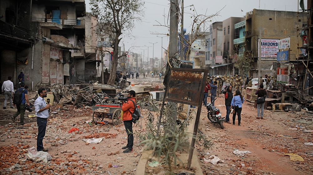 In this Thursday, Feb. 27, 2020 photo, a television reporter, left, reports from a street vandalized in Tuesday's violence in New Delhi, India. Reporting in India has never been without its risks, but