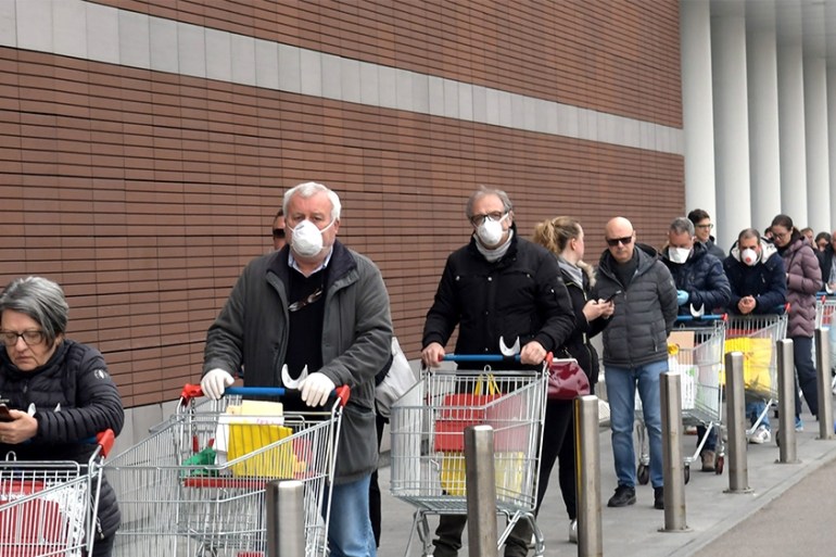 epaselect epa08289489 People wearing protective face masks lined up at a safe distance in front of a supermarket in Milan, Italy, 12 Mrch 2020. Tougher lockdown measures kicked-in in Italy on the day