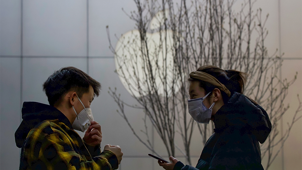 Masked shoppers stand near the Apple logo in Beijing, China. Tech giant Apple has reopened some stores in China but it’s stock value has fallen two days in a row as worries grow that the viral outbrea