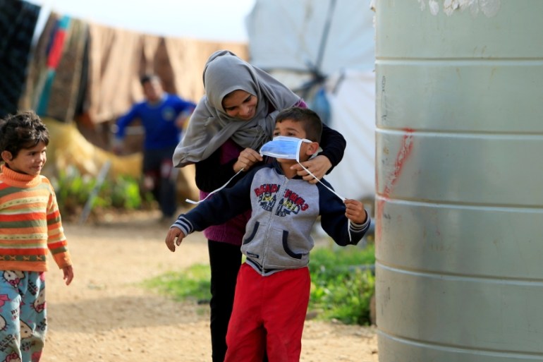 A Syrian refugee woman puts a face mask on a boy as a precaution against the spread of coronavirus, in al-Wazzani area in southern Lebanon