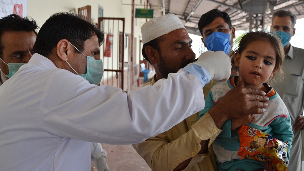 A man holds his daughter as a health official checks her body temperature amid concerns over the spread of the COVID-19 novel coronavirus at Peshawar railway station in Peshawar on March 17, 2020. (Ph