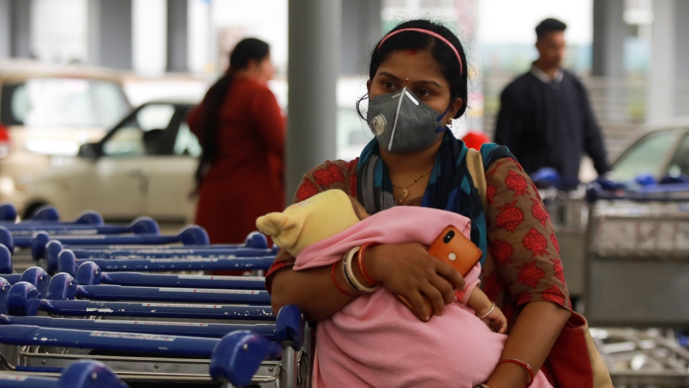 A passenger wearing a protective mask holds a baby as she waits outside an airport following an outbreak of the coronavirus disease (COVID-19), in New Delhi