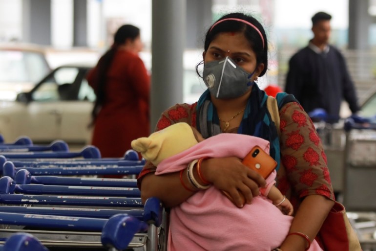 A passenger wearing a protective mask holds a baby as she waits outside an airport following an outbreak of the coronavirus disease (COVID-19), in New Delhi
