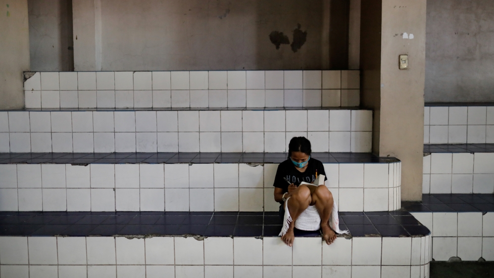 A woman wearing a protective face mask reads the Bible in a gymnasium which turned into a shelter for the homeless following the enforcement of a community quarantine in Manila