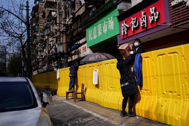 Residents pay for groceries over barriers set up to ring fence a wet market on a street in Wuhan
