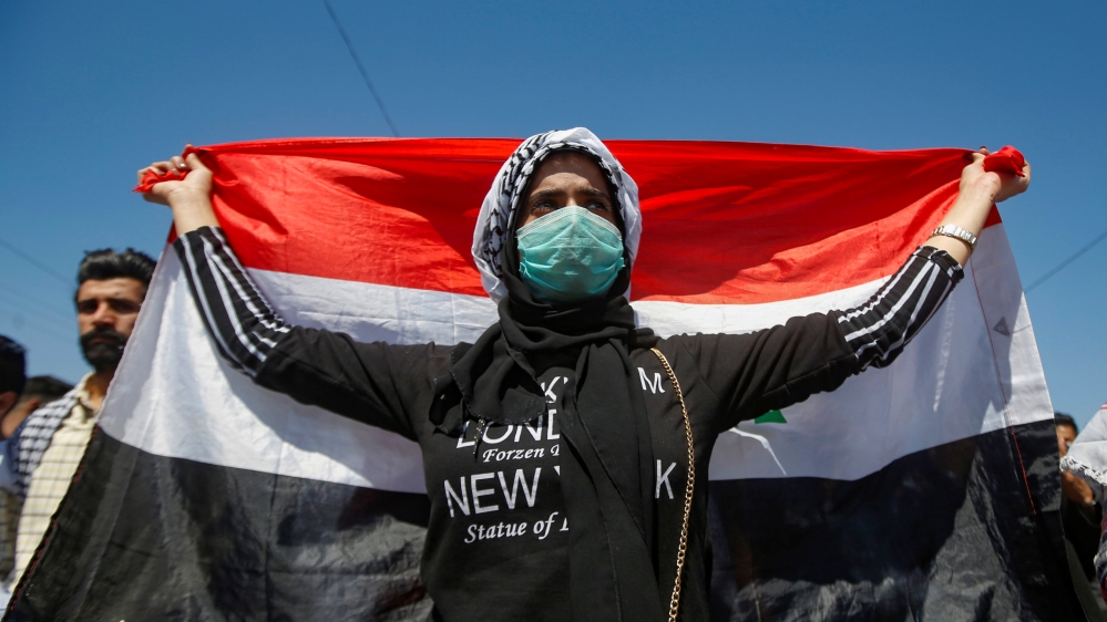 A student wears a protective face mask, following the outbreak of the new coronavirus, as she carries the Iraqi flag during ongoing anti-government protests in Basra