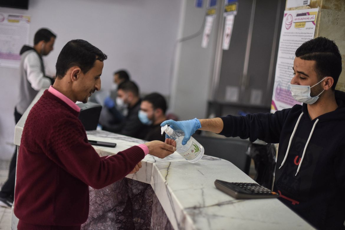 An employee at a currency exchange gives a customer a squirt of hand sanitizer, now a common ritual in Gazan stores.