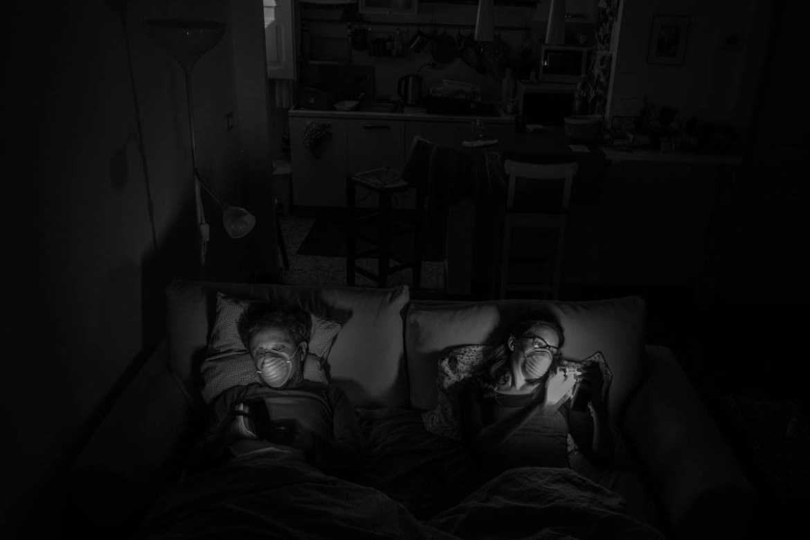 On the sofa bed before watching a movie. Most of the time when they are together Alessio and Marta have to wear masks. At night they sleep in separate beds.
