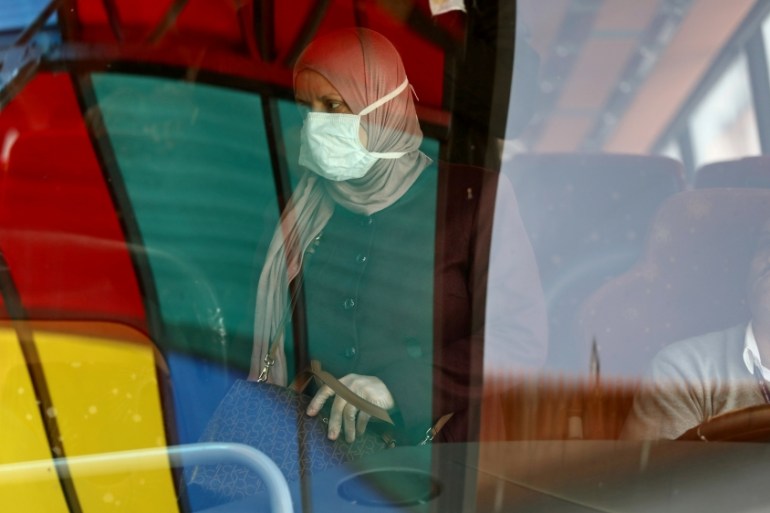 A Palestinian woman wearing a mask as a preventive measure against coronavirus, alights from a bus upon her return from abroad, at the Israeli-controlled Allenby Bridge crossing in Jericho, in the Is