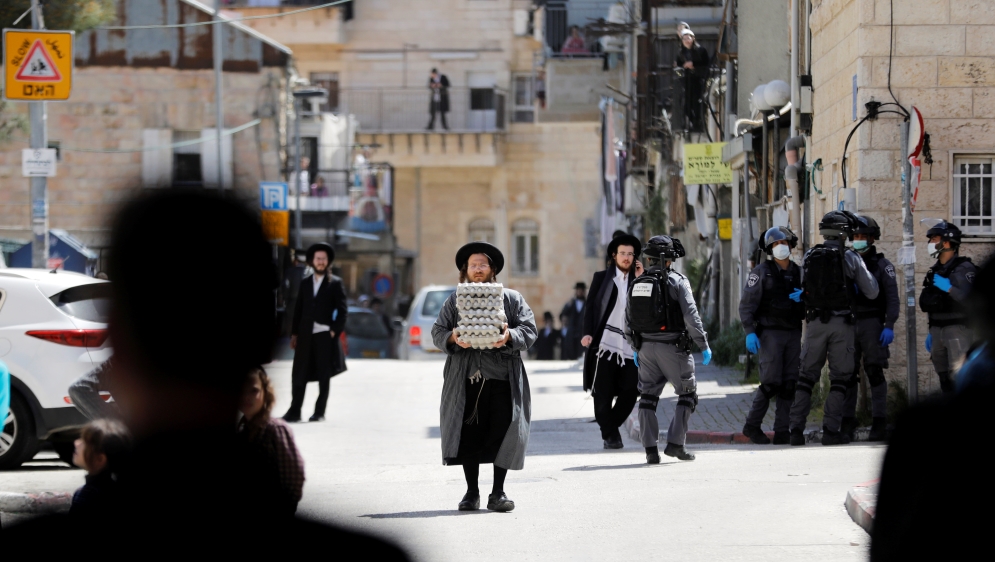 An ultra-Orthodox Jewish man carries trays of eggs as Israeli police patrol nearby to enforce government restrictions set in place to curb the spread of the coronavirus (COVID-19), in Mea Shearim neig