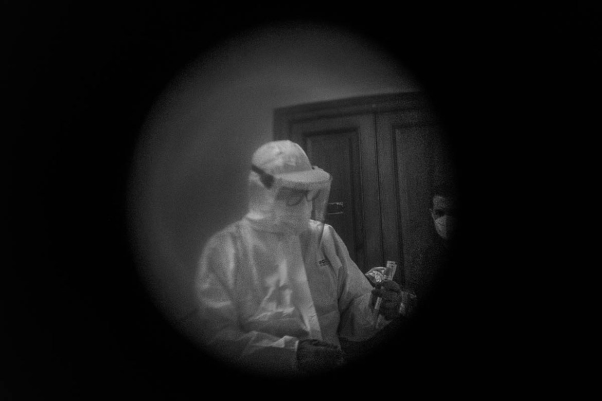 Two nurses photographed through the peephole outside the door of their house while preparing the swab. The nurses of the regional health department is turning all around the cities the houses where su