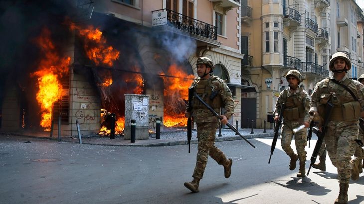 Lebanese army soldiers run in front of a Credit Libanais Bank that was set on fire by anti-government protesters, in the northern city of Tripoli, Lebanon, Tuesday, April 28, 2020. Hundreds of angry L