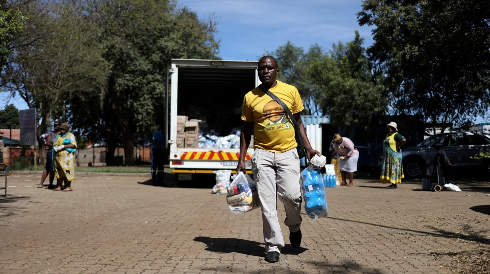 A man wearing a t-shirt with the face of South Africa's president, Cyril Ramaphosa leaves as people distribute food parcels prepared by the local government to vulnerable residents during a 21-day loc