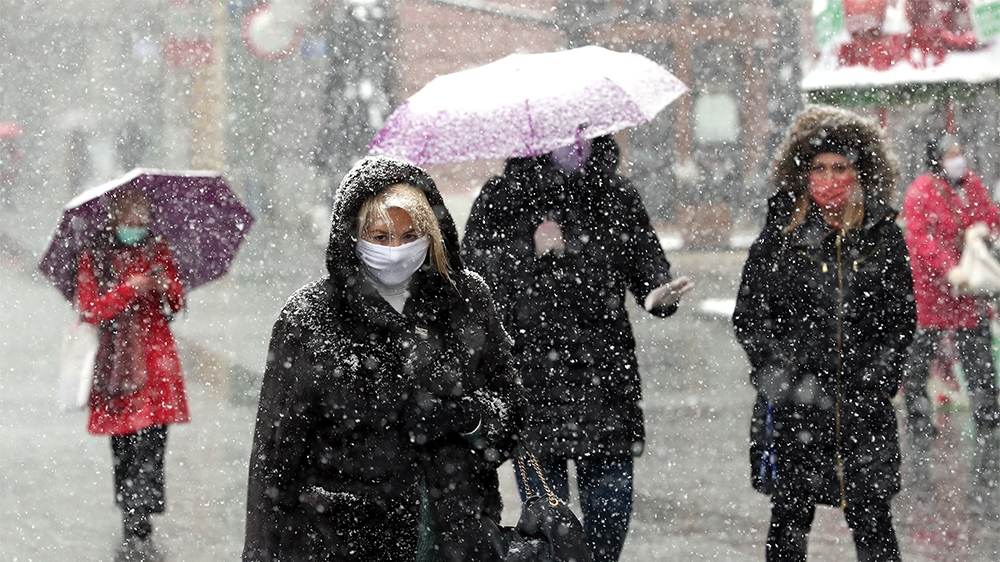 epa08334217 People wearing face masks hold up umbrellas to shield themselves from heavy snowfall in Sarajevo, Bosnia and Herzegovina, 31 March 2020. According to latest figures by WHO on 30 March, a t
