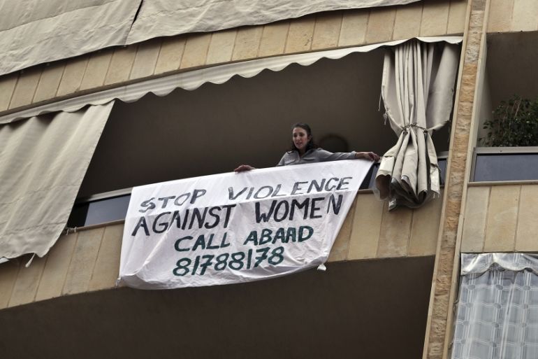 A woman hangs a banner from her balcony with the number of a domestic violence hotline during a national lockdown aimed at stemming the spread of coronavirus, in Beirut, Lebanon, Thursday, April 16, 2