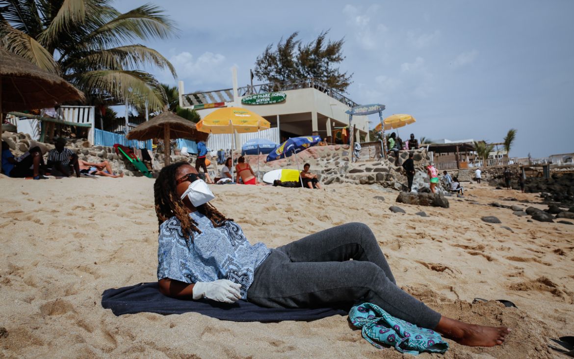 A beachgoer wears clothes, a protective face mask and gloves to a Dakar beach while remaining meters apart from others. Public spaces have remained opened but gatherings of more than 10 people are ban