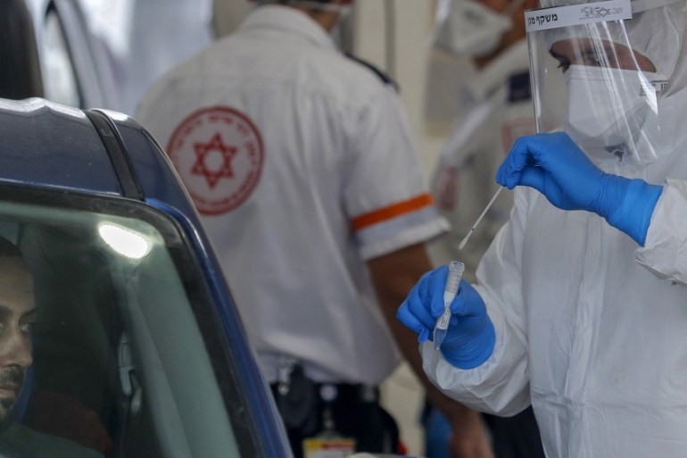 A Paramedic with Israel''s Magen David Adom (Red Shield of David) national emergency medical service, puts a swab into a tube after using it to test a man for COVID-19, at a drive-thru testing site in