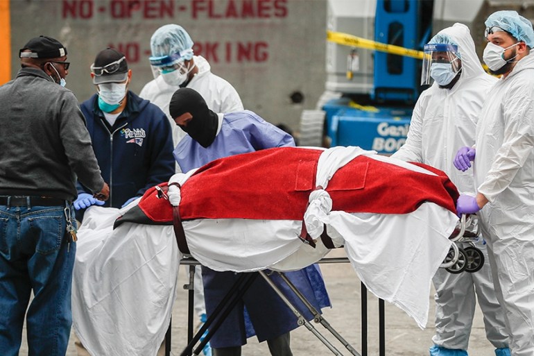 A body wrapped in plastic that was unloaded from a refrigerated truck is handled by medical workers wearing personal protective equipment due to COVID-19 concerns, Tuesday, March 31, 2020, at Brooklyn