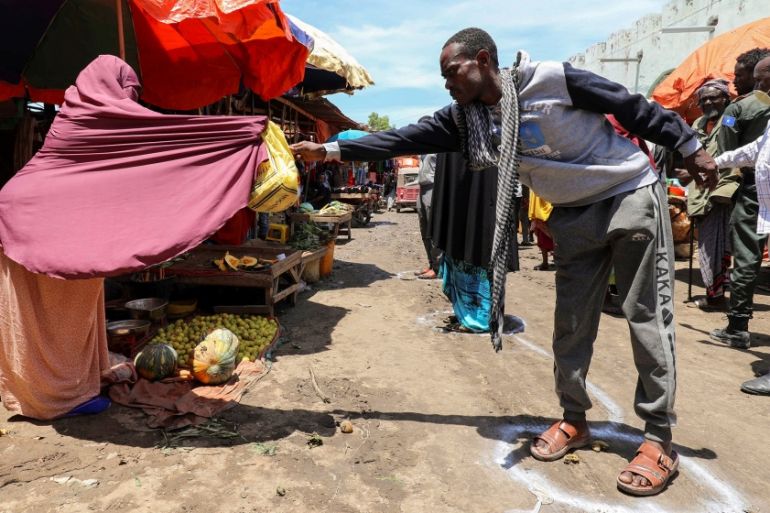 A Somali woman sells fruits to a customer standing at a social distancing signage, as a measure to stem the growing spread of the coronavirus disease (COVID-19) outbreak, at the market centre in Hamar