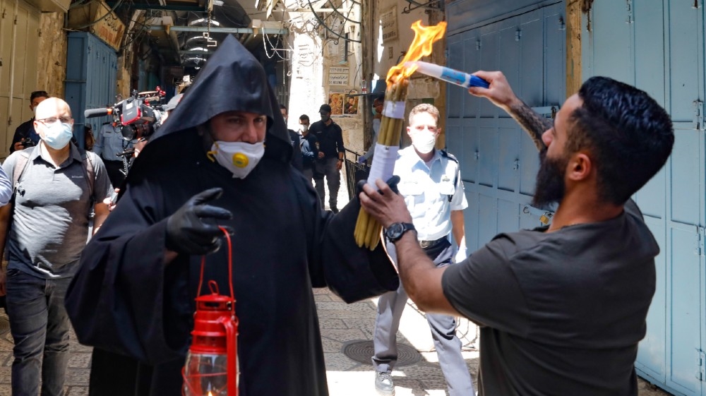 An Armenian priest wearing a protective mask and gloves passes on the Holy Fire lit in the church of the Holy Sepulchre, as very few Orthodox Christians gather in J