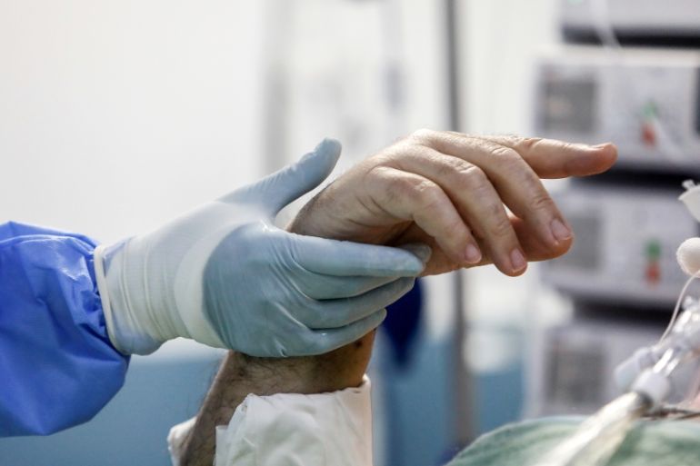 An intubated patient tries to gesture at a medical worker holding his hand at the intensive care unit (ICU) of the Sotiria hospital, following the coronavirus disease (COVID-19) outbreak, in Athens, G