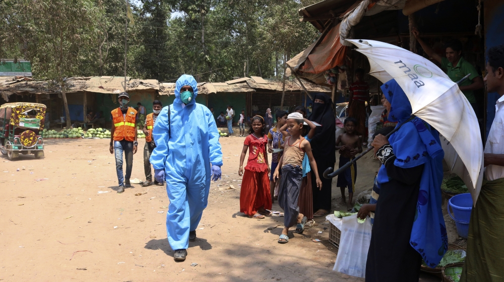 In this April 15, 2020, photograph, a health worker from an aid organization walks wearing a hazmat suit at the Kutupalong Rohingya refugee camp in Cox's Bazar, Bangladesh. There's been little if any 