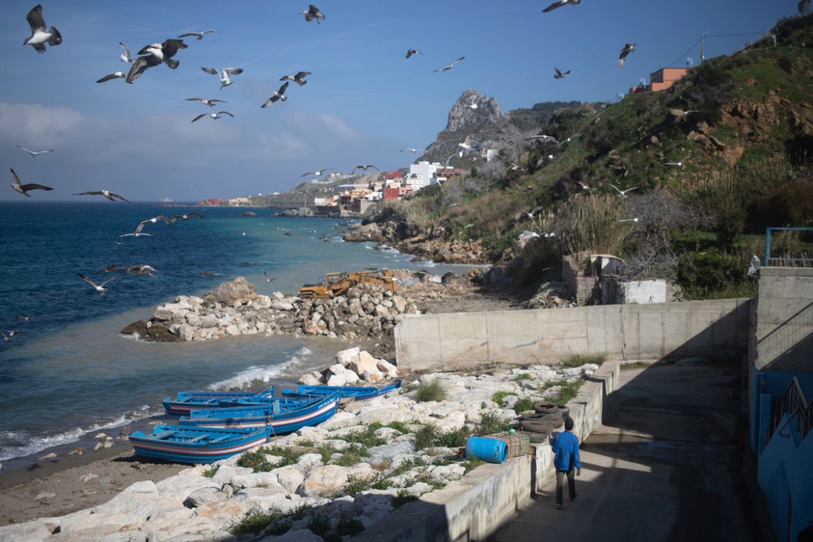 In this Tuesday, Feb. 11, 2020 photo, a seagulls fly as a fisherman walks towards a beach in the village of Belyounech, where the the first Moroccan female fishing cooperative was started, on the coas