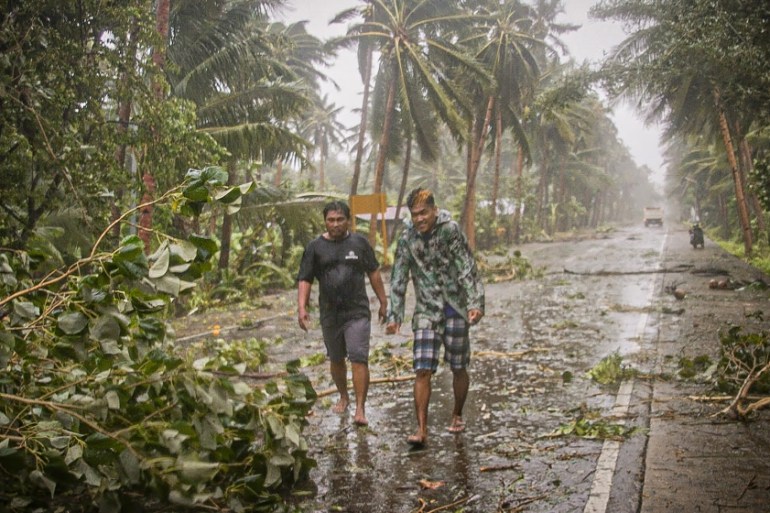 Residents brave rains and strong wind as they walk past uprooted trees along a highway in Can-avid town, Eastern Samar province, central Philippines on May 14, 2020, as Typhoon Vongfong makes landfall