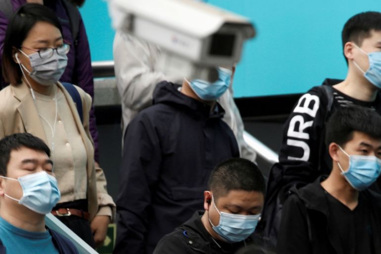 People wearing face masks are seen near a surveillance camera inside a subway station during morning rush hour in Beijing