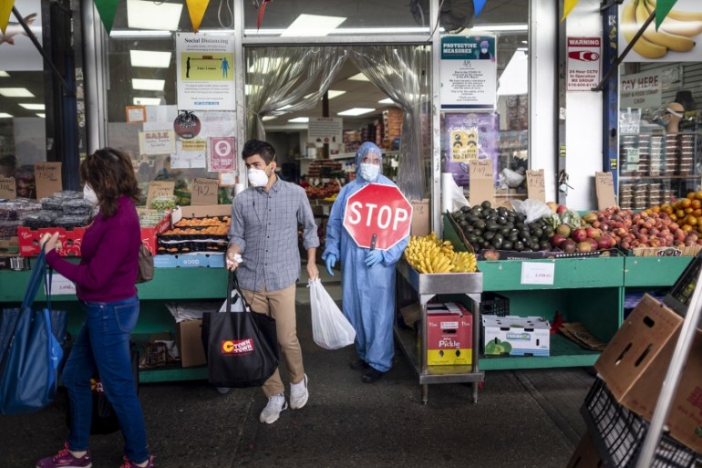 A worker wearing a full body suit holds a STOP sign in front of a Food market as he manages the flow of the customers on May 18, 2020 in the Jackson Heights neighbourhood of Queens in New York City. J