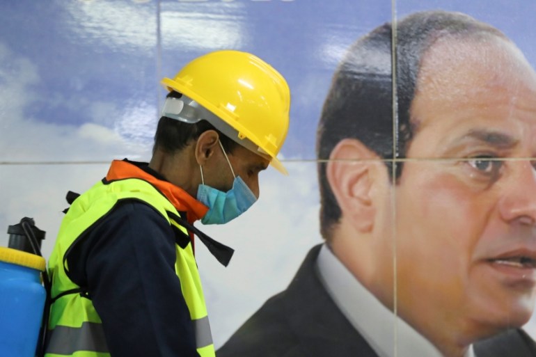 A member of medical team is seen beside a banner for the Egyptian President Abdel Fattah el-Sisi, as he sprays disinfectant at the Al Shohadaa "Martyrs" metro station in Cairo