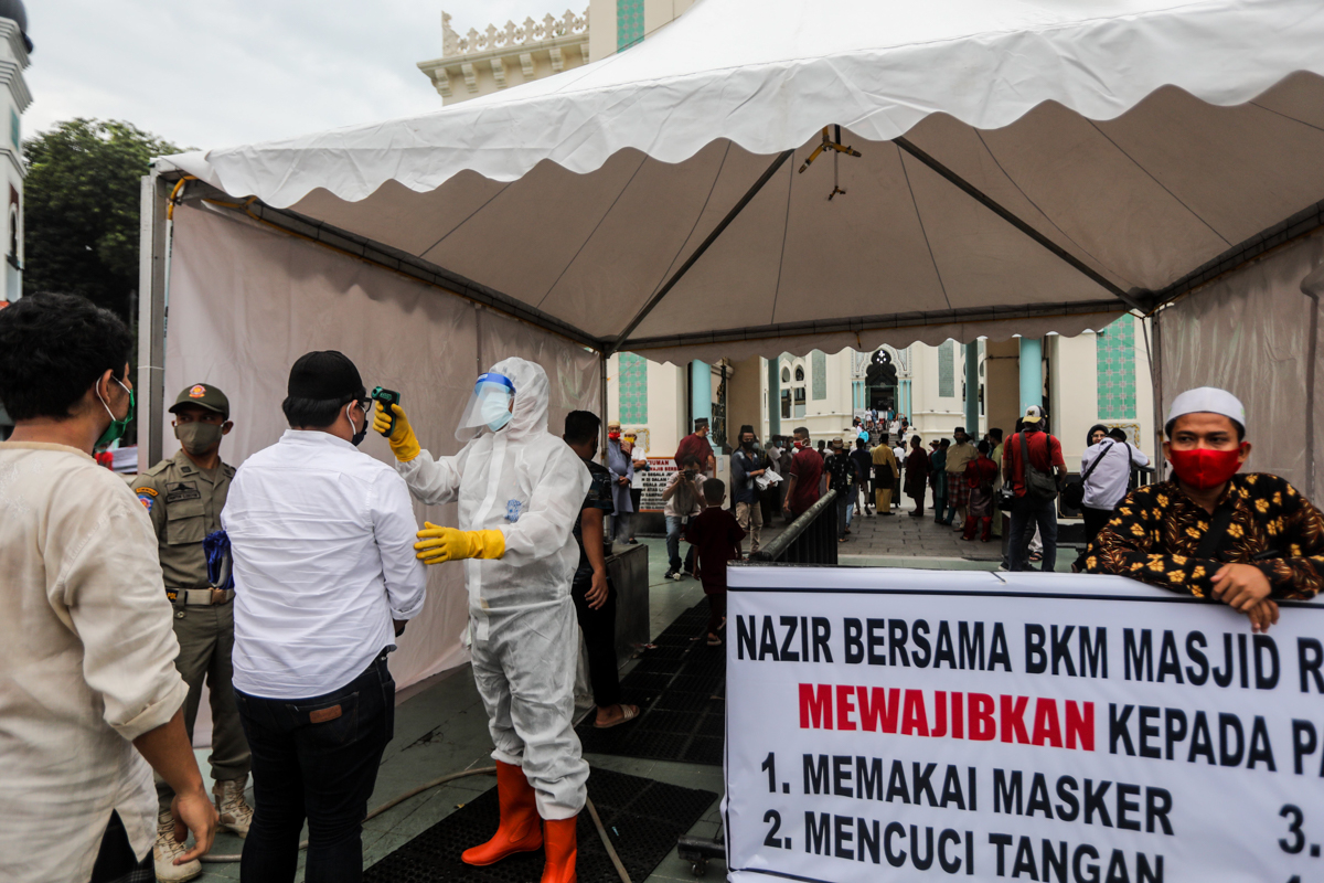 epa08440338 An health official wearing a protective suit checks the body temperatures of people before attending Eid al-Fitr prayers amid the coronavirus pandemic, at Al Mashun Grand Mosque in Medan, 