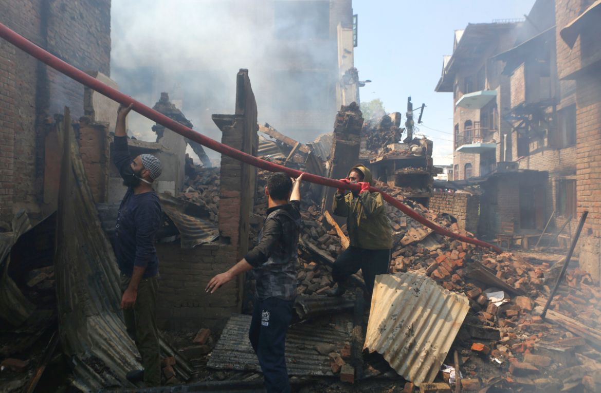 epa08431593 A Fire serviceman and Kashmiri Muslims hold a water hose to douse a fire in houses which were damaged during a gunfight between Indian security forces and militants in the downtown area of