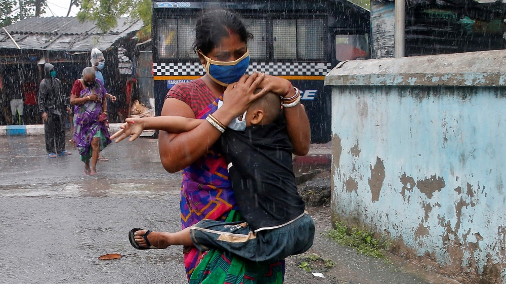 A woman carries her son as she tries to protect him from heavy rain while they rush to a safer place, following their evacuation from a slum area before Cyclone Amphan makes its landfall, in Kolkata, 