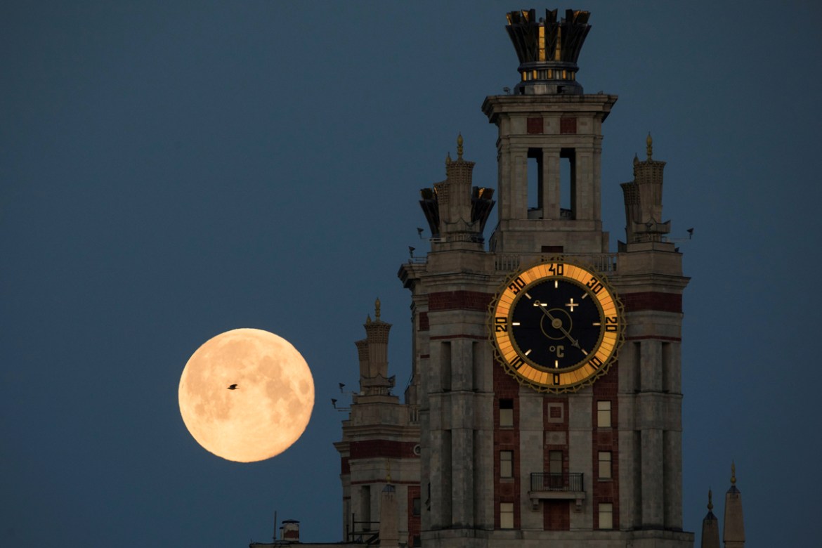 A bird flies past the full moon, also known as the Supermoon or Flower Moon, as it is seen behind the Lomonosov Moscow State University in Moscow, Russia May 8, 2020. REUTERS/Shamil Zhumatov TPX IMAGE