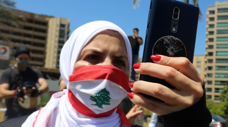 A demonstrator, wearing a face mask as a preventive measure against the spread of the coronavirus disease (COVID-19) and depicting the national flag, uses her mobile during a protest against a controv