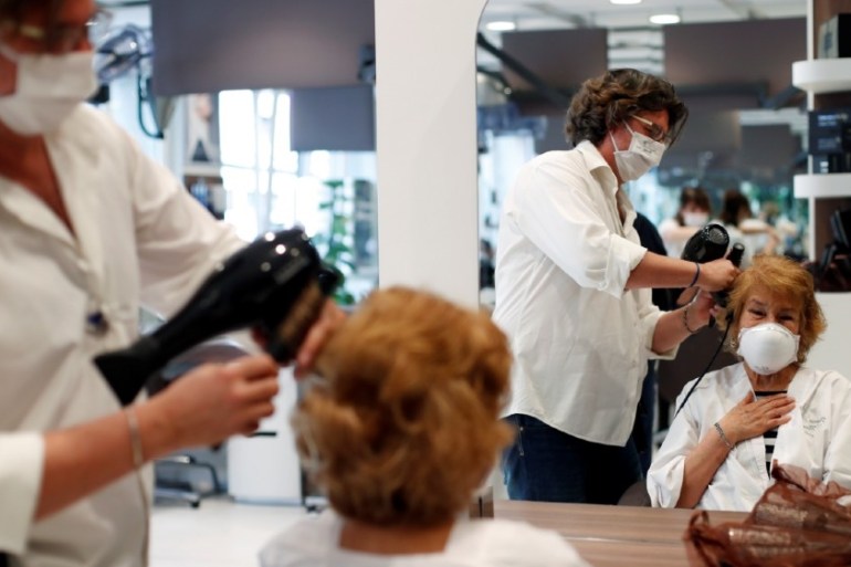 A woman wearing a protective mask serves a customer in a hair salon, as Italy eases some of the lockdown measures put in place during the coronavirus disease (COVID-19) outbreak