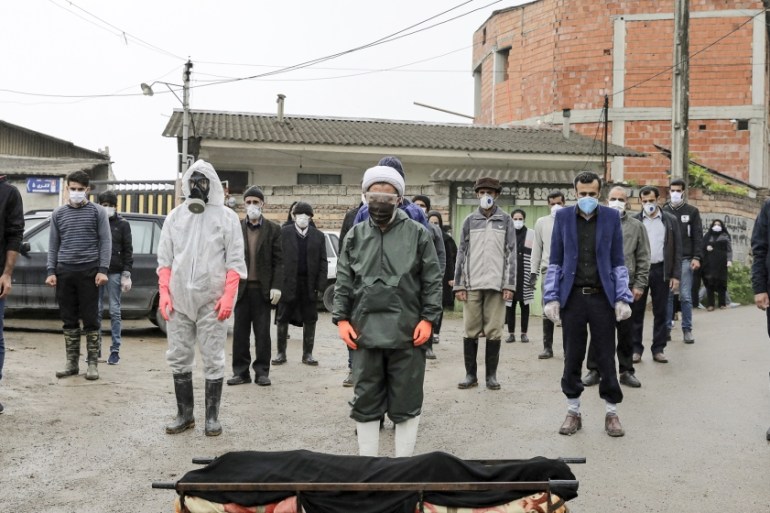 Mourners wearing protective clothing, face masks and gloves, pray over the body of a victim who died after being infected with the new coronavirus, in the outskirts of the city of Babol, in north of I