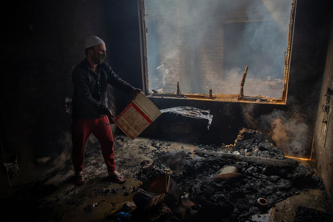 A Kashmiri man douses a fire in a house which was damaged in a gun-battle in Srinagar, Indian controlled Kashmir, Tuesday, May 19, 2020. Indian government forces killed two rebels in disputed Kashmir
