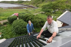 Brian Gardner and Ben Cormack fit solar thermal water heaters onto the roof of a cottage on the island of Eigg, Inner Hebrides, Scotland