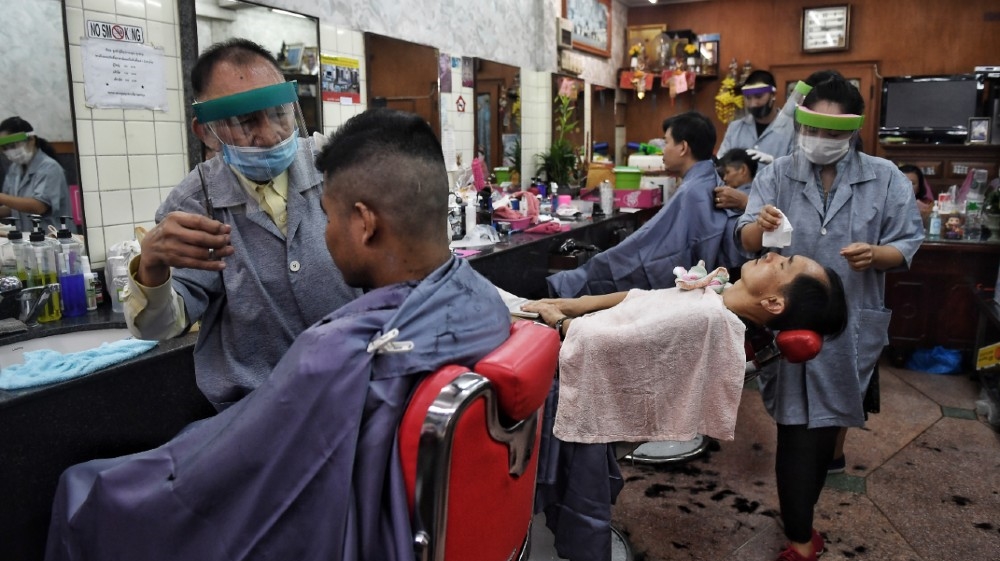 Hairdressers wear face shields and masks as they tend to customers at a barbershop in Bangkok on May 3, 2020, after it reopened due to an easing of measures to combat the spread 
