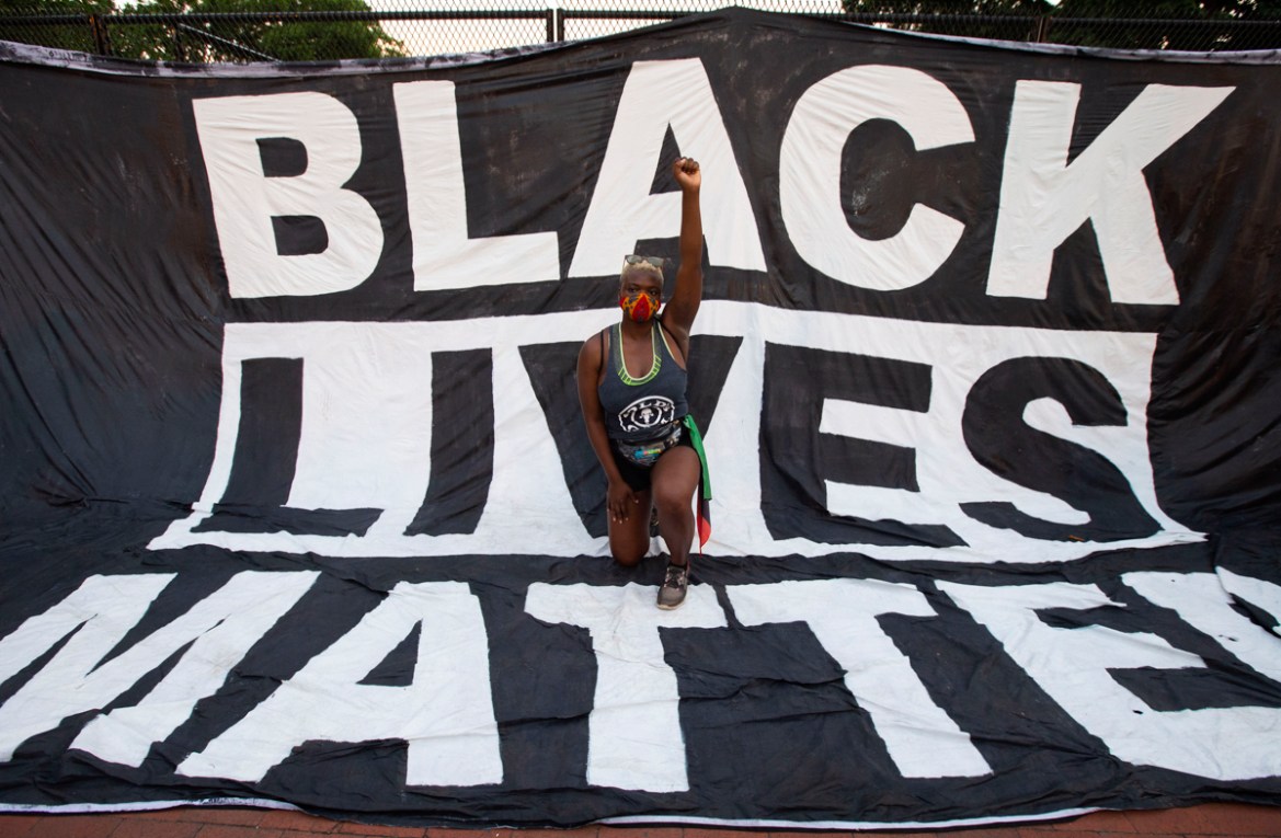 A protester kneels and holds up a fist on a giant Black Lives Matter banner near the White House during a demonstration against racism and police brutality, in Washington, DC on June 6, 2020. - Demons