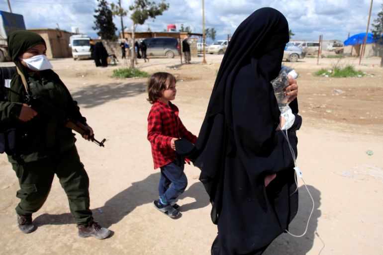 A fighter of Syrian Democratic Forces (SDF) walks with the wife of an Islamic State fighter, who holds her sick baby, at al-Hol displacement camp in Hasaka governorate