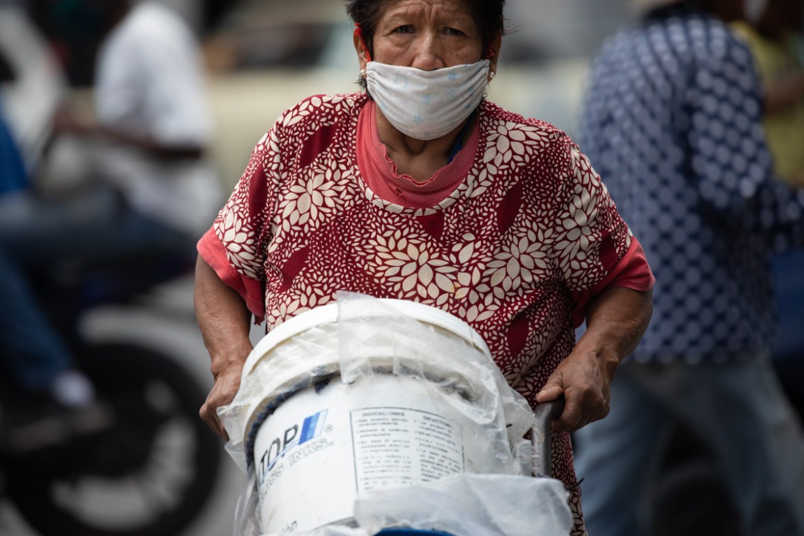 A woman, wearing a protective face mask, pushes a dolly of containers filled with water, in Caracas, Venezuela, Saturday, June 20, 2020, during a relaxation of restrictive measures amid the new corona