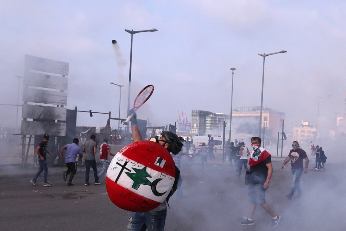 An anti-government protester throws back tear gas at riot policemen with a tennis racket during ongoing protests against the Lebanese government, in downtown Beirut, Lebanon, Saturday, June 6, 2020. H