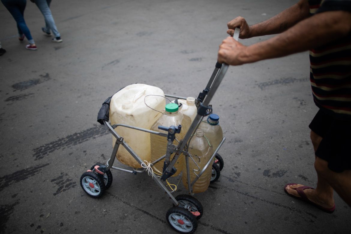 A man pushes a stripped down baby stroller with containers he filled with water that he collected from a street faucet, in Caracas, Venezuela, Saturday, June 20, 2020. Water service in Venezuela has g