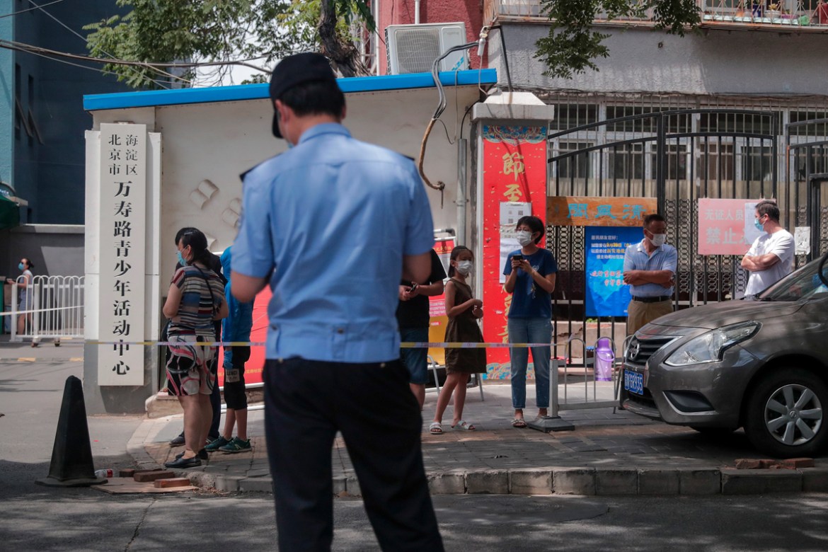 A police officer stands on duty as people wearing protective face masks to help curb the spread of the new coronavirus stand watch behind a barricade line after several residential buildings was locke